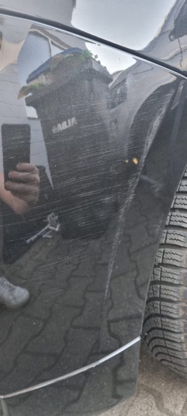 Reflexion eines Fahrzeugs mit einer unebenen Oberfläche und einem Reifen im Hintergrund.